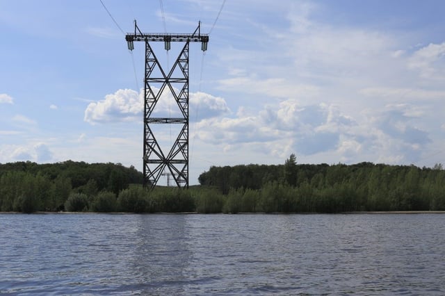 Metal pillar stands on the banks of a large body of water.